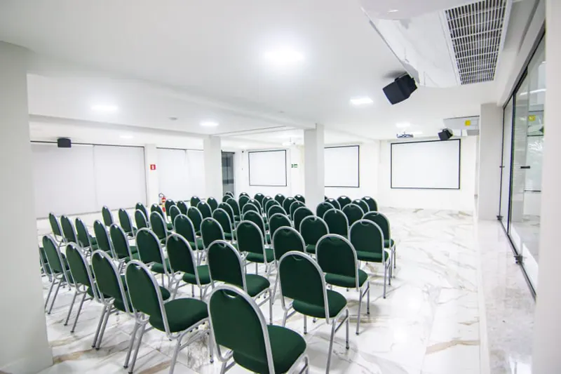 Auditório do Gaeta Hotel, claro, com fileiras de cadeiras estofadas voltadas para a frente