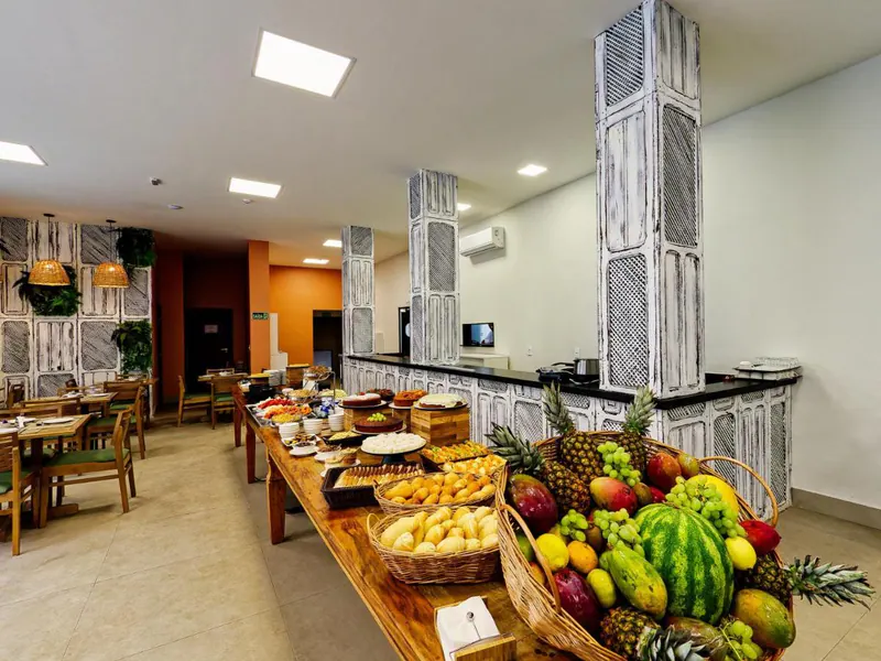 Buffet do café da manhã do hotel, com pães, bolos e uma gamela de frutas tropicais