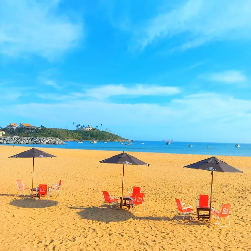 Guarda-sóis e cadeiras na areia dourada, com o mar azul e um morro ao fundo