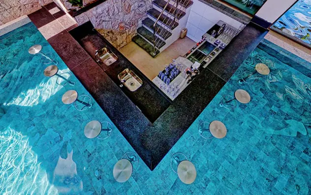 Recanto dentro da piscina, visto do alto: bancos submersos em volta de um balcão de pedra escura